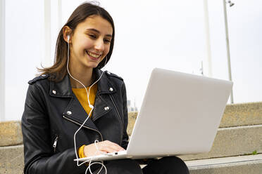 Junge Frau, die mit ihrem Laptop Musik hört. - CAVF79982