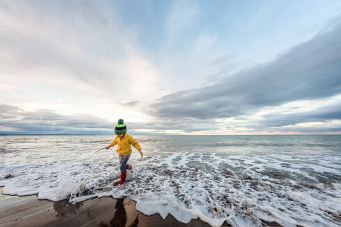 Vorschulkind läuft mit Stiefeln und Hut im Wasser in Neuseeland - CAVF80004