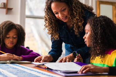 Mature woman assisting daughters studying at table in living room - CAVF80016