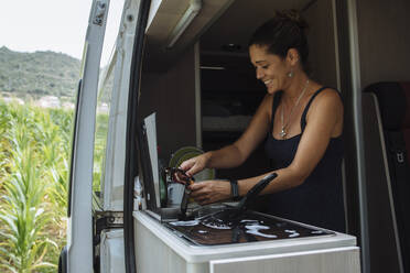 Frau mit Ohrringen beim Geschirrspülen im Wohnmobil während eines Urlaubs. - CAVF80065