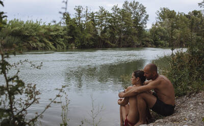 Pärchen in Badeanzügen, das sich im Urlaub am Flussufer umarmt. - CAVF80066