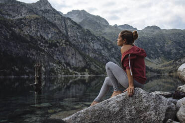 Woman with bun sitting on a rock by a lake during a trip. - CAVF80069