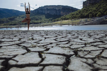 Woman balancing on one leg at the edge of a lake. - CAVF80074