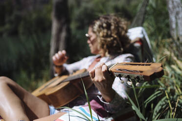 Frau mit Sonnenbrille spielt Gitarre in einer Hängematte. - CAVF80083