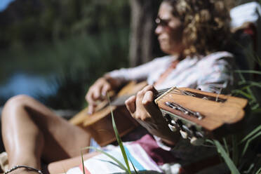 Frau mit Sonnenbrille spielt Gitarre in einer Hängematte. - CAVF80084