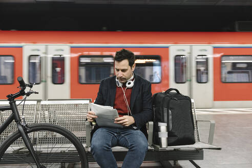 Geschäftsmann mit Fahrrad, der in einer U-Bahn-Station sitzend Dokumente liest, Frankfurt, Deutschland - AHSF02342