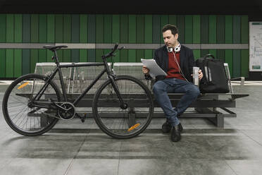 Geschäftsmann mit Fahrrad, der am Bahnsteig einer U-Bahn-Station sitzt und Dokumente liest, Frankfurt, Deutschland - AHSF02343