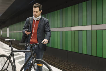 Geschäftsmann mit Fahrrad Textnachrichten auf dem Handy, während er in einer U-Bahn-Station steht - AHSF02347