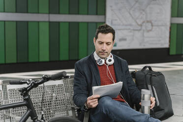 Geschäftsmann mit Fahrrad, der am Bahnsteig einer U-Bahn-Station sitzt und Dokumente liest, Frankfurt, Deutschland - AHSF02363