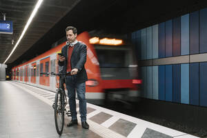 Geschäftsmann mit Fahrrad Textnachrichten auf dem Smartphone, während er auf dem Bahnsteig vor einem U-Bahn-Zug steht - AHSF02364