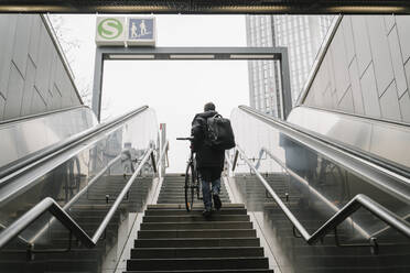 Businessman with bicycle walking on staircase while moving out of subway station in city - AHSF02365