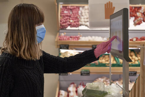Frau mit Maske wiegt Gemüse auf einer Waage im Supermarkt - VEGF01968