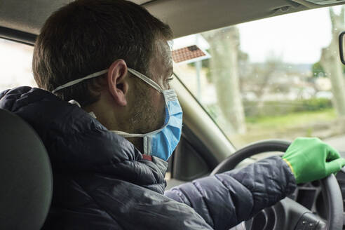 Man wearing mask and gloves driving car in city - VEGF01971