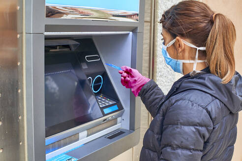 Woman wearing mask using credit card at ATM during pandemic situation - VEGF01973