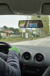 Mann mit Maske und Handschuhen fährt Auto und spiegelt sich im Rückspiegel in der Stadt - VEGF01975