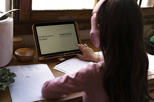 Mädchen mit Kopfhörern, das beim Lernen von Comics zu Hause Sprachen auf einem digitalen Tablet übersetzt - ERRF03530