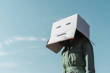 Woman with cardboard box on her head standing against sky - AFVF06132