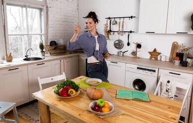 Young and beautiful housewife woman cooking in a white kitchen - CAVF80164