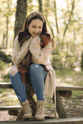 Junge Frau sitzt auf einem Picknicktisch umgeben von einem Wald - CAVF80459