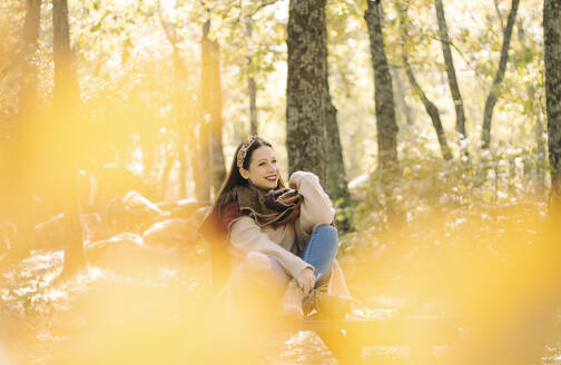 Junge Frau sitzt auf einem Picknicktisch umgeben von einem Wald - CAVF80460