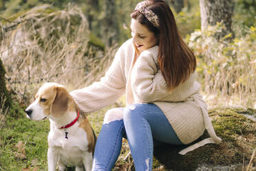 Lächelnde junge Frau, die bei einem Spaziergang neben ihrem Hund sitzt - CAVF80464
