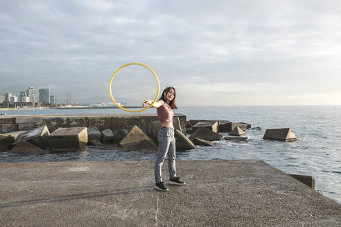 Glückliche Frau spielt mit Hula-Hoop-Reifen am Hafen - XLGF00077