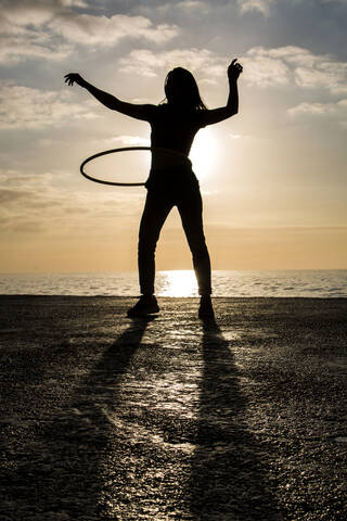 Glückliche Frau spielt mit Hula-Hoop-Reifen am Hafen bei Sonnenuntergang, lizenzfreies Stockfoto