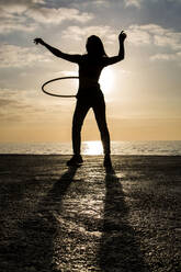 Happy woman playing with hula hoop at harbour during sunset - XLGF00084