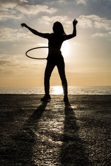 Glückliche Frau spielt mit Hula-Hoop-Reifen am Hafen bei Sonnenuntergang - XLGF00084