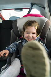Porträt eines lachenden kleinen Mädchens, das auf einem Kindersitz im Auto sitzt - MGIF00900