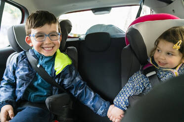 Porträt eines glücklichen kleinen Jungen und seiner jüngeren Schwester, die im Auto sitzen und sich an den Händen halten - MGIF00901