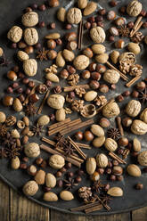 Star anise, cinnamon sticks and various nuts lying on rustic baking sheet - ASF06615