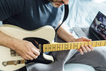 Mann lernt mit Laptop online E-Gitarre spielen - JCMF00622