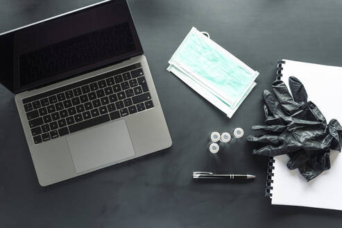 Directly above shot of medical samples with protective wear and spiral notebook by laptop on table - JCMF00632