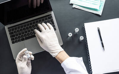 Direkt über der Aufnahme eines Wissenschaftlers, der eine medizinische Probe analysiert, während er einen Laptop am Schreibtisch im Labor benutzt - JCMF00634