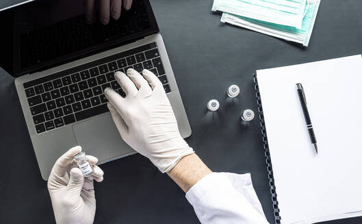 Directly above shot of scientist analyzing medical sample while using laptop at desk in laboratory - JCMF00634