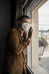 Mann mit Schutzmaske und Blick aus dem Fenster - RCPF00231