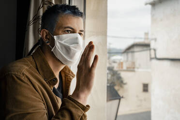 Man wearing protective mask and looking out of the window - RCPF00233