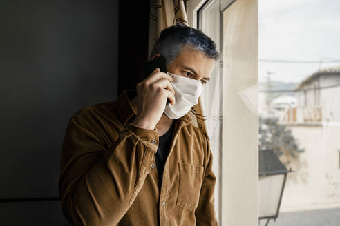 Mann mit Schutzmaske und Blick aus dem Fenster - RCPF00236