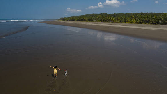 Unbekümmerte junge Frau geht mit ihrem Hund am Strand spazieren, Costa Rica - AMUF00090