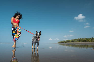 Unbekümmerte junge Frau geht mit ihrem Hund am Strand spazieren, Costa Rica - AMUF00094
