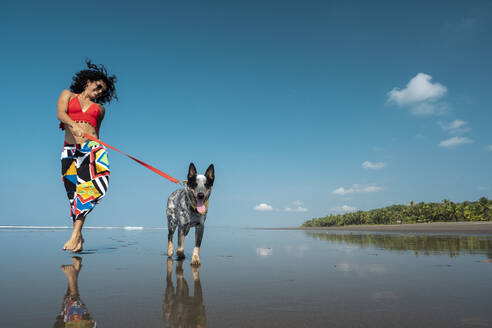 Unbekümmerte junge Frau geht mit ihrem Hund am Strand spazieren, Costa Rica - AMUF00094