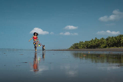 Unbekümmerte junge Frau geht mit ihrem Hund am Strand spazieren, Costa Rica - AMUF00095