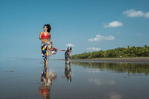 Junge Frau geht mit ihrem Hund am Strand spazieren, Costa Rica - AMUF00096