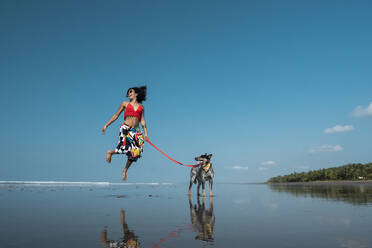 Carefree young woman taking her dog for a walk at the beach, Costa Rica - AMUF00097