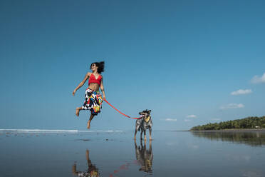 Unbekümmerte junge Frau geht mit ihrem Hund am Strand spazieren, Costa Rica - AMUF00097