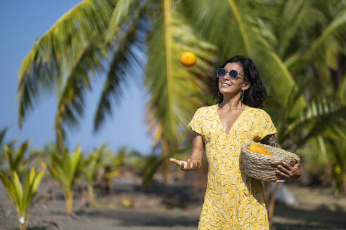 Junge Frau hält einen Obstkorb am Strand, Costa Rica - AMUF00099