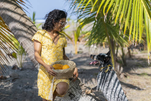 Junge Frau mit einem Obstkorb am Strand mit ihrem Hund, Costa Rica - AMUF00100