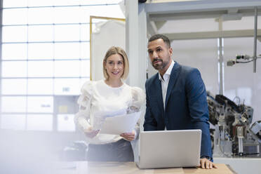 Businessman and young woman with papers and laptop in a factory - DIGF09890