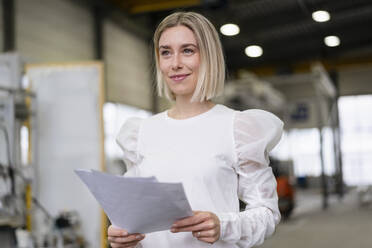 Portrait of a smiling young woman holding papers in a factory - DIGF09893